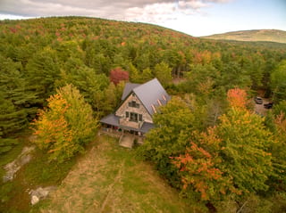 Deep Charcoal Interlock Cedar Shingle aluminum roof on a two-storey Cape Cod home with dormers among tall trees, Bar Harbor, Maine