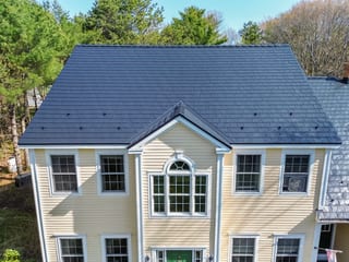 Black Interlock Slate aluminum roof on a yellow two-storey Colonial home with dormers among tall, Brunswick, Maine