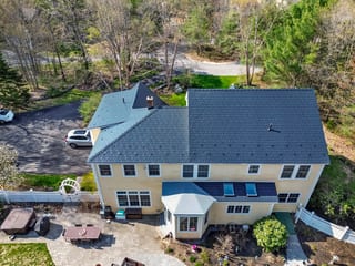 Black Interlock Slate aluminum roof on a two-storey home with a metal roof among tall trees, Brunswick, Maine