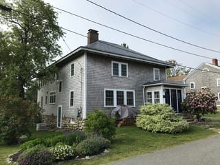 Two-story Colonial home in Rockport MA with Interlock charcoal grey aluminum slate metal roof, brick chimney, cedar shingle siding, and blooming landscaping.