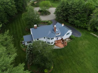 Aerial rear view of a large Colonial home in Topsfield, MA with a complex deep charcoal Interlock aluminum slate metal roof, two chimneys, and a rear wood deck.