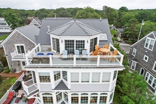 Aerial front view of a 3-story coastal shingle-style home in Sagamore Beach, MA featuring a multi-hip Interlock aluminum slate roof in Deep Charcoal with a rooftop deck.