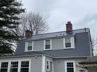 Two-story Colonial home in Walpole, MA with a deep charcoal Interlock aluminum slate mansard roof, two brick chimneys, and three dormers.