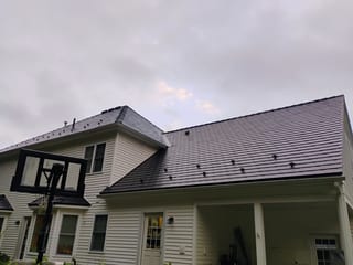 Two-story Colonial home with a complex black Interlock aluminum slate metal roof featuring snow guards, a dormer, and covered rear porch.