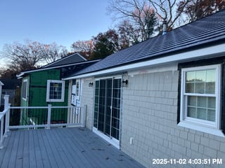 Rear elevation of a Cape Cod home with a newly installed Interlock deep charcoal cedar shingle metal roof on a deck-level view, mid-renovation.