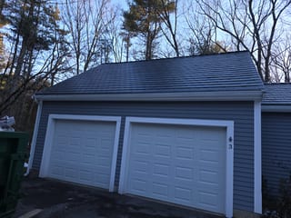 Front elevation of a detached two-car garage with Interlock Deep Charcoal aluminum slate metal roofing and hip roof, blue-gray vinyl siding, Westford MA.
