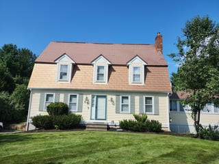 Aged Copper Interlock Shingle aluminum roof on a yellow two-storey Colonial home with dormers among tall, Wrentham, Massachusetts