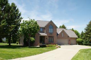 Weathered Interlock Shake aluminum roof on a tan two-storey home with dormers among tall pines, Mendota Heights, Minnesota
