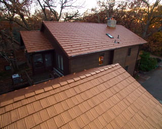 Aged Copper Interlock Shake aluminum roof on a two-storey home with dormers among tall trees, Bloomington, Minnesota