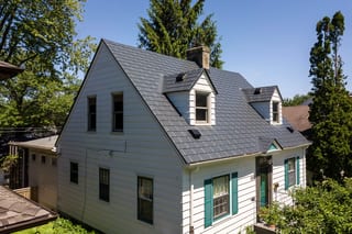Deep Charcoal Interlock Slate aluminum roof on a white two-storey Cape Cod home among tall trees, St Paul, Minnesota