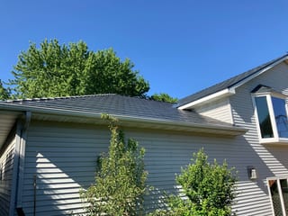 Deep Charcoal Interlock Slate aluminum roof on a grey two-storey home with a metal roof among tall trees, Rochester, Minnesota