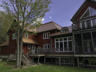 Aged Copper Interlock Cedar Shingle aluminum roof on a red two-storey home with a metal roof among tall pines, Hanwell, New Brunswick