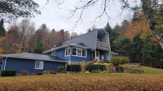 Black Interlock Slate aluminum roof on a blue one-storey cottage with dormers among tall pines, Utopia, New Brunswick
