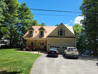 Aged Copper Interlock Slate aluminum roof on a yellow two-storey colonial home with dormers among tall, Rindge, New Hampshire