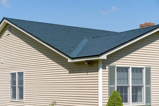 Hunter Green Interlock Slate aluminum roof on a beige one-storey home with a green metal roof among green, Sanbornville, New Hampshire