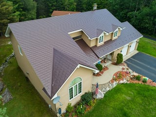 Colonial Brown Interlock Slate aluminum roof on a brown single-storey colonial home among tall trees, Milan, New Hampshire