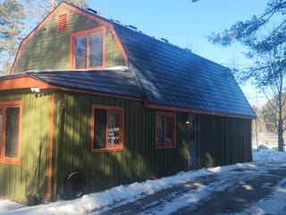 Deep Charcoal Interlock Slate aluminum roof on a green home with a black roof among tall trees, Wilmot, New Hampshire