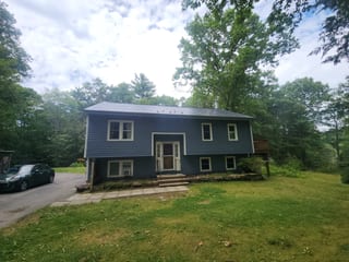 Two-story colonial home in Bow, NH with Interlock deep charcoal aluminum slate metal roof, blue vinyl siding, and wooded backdrop.