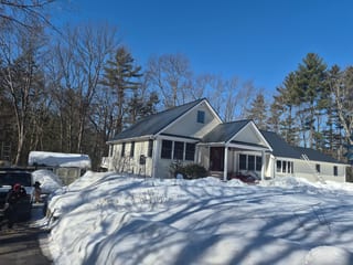 Cape Cod home in Epping NH with Interlock deep charcoal cedar shingle aluminum metal roof, front-left view amid heavy winter snow.