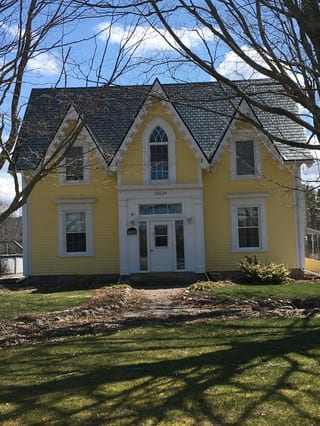 Black Interlock Slate aluminum roof on a yellow two-storey home with dormers among tall pines, Paradise, Nova Scotia
