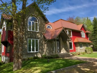 Black Interlock Slate aluminum roof on a red two-storey home with dormers among tall pines, Reids Hill (Shelburne), Nova Scotia