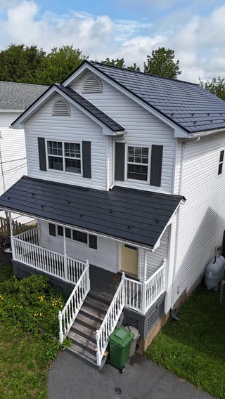 A white colonial home with a black metal roof and a skylight