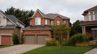Tudor Brown Interlock Slate aluminum roof on a brown two-storey home with dormers among tall trees, Barrie, Ontario