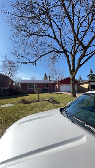 Ranch-style brick home in Toronto with Interlock Musket Grey aluminum slate metal roof, low-pitched profile, attached garage, and mature bare tree in foreground.
