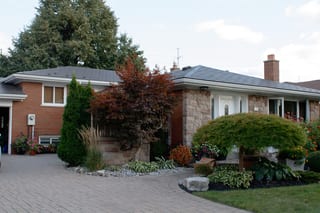 Ranch-style brick and stone home in Scarborough with Interlock Tudor Brown aluminum slate roof, hip profile, brick chimney, and lush landscaped front yard.