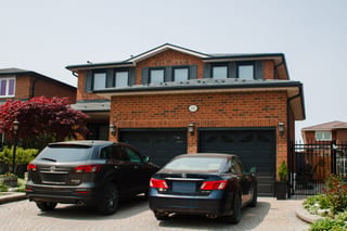 Two-storey brick home in Woodbridge ON with Interlock deep charcoal aluminum slate metal roofing, dormers, and double dark garage doors.