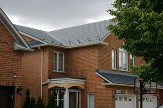 Two-storey suburban brick townhome with deep charcoal Interlock aluminum slate metal roof featuring snow guards on a complex multi-hip roofline.
