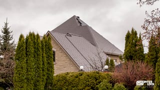 Large two-storey stone home with a steeply pitched multi-hip Interlock aluminum slate roof in Tudor Brown, featuring skylights and complex valleys.