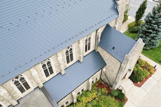 Aerial view of a Gothic stone church in Toronto with a deep charcoal Interlock aluminum slate roof featuring snow rails, complex valleys, and Gothic arched windows.
