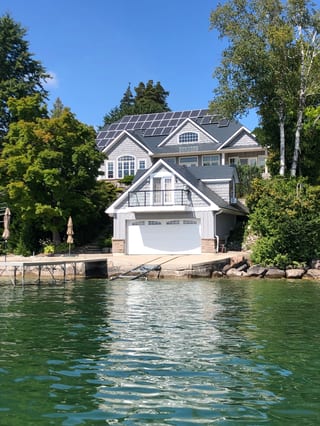 Large Craftsman lakefront home in Shanty Bay, ON with deep charcoal Interlock aluminum slate roofing, multiple dormers, and solar panels viewed from the water.