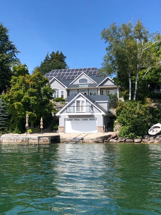 Large Craftsman lakefront home in Shanty Bay, ON with deep charcoal Interlock aluminum slate roof, solar panels, and a boathouse at water's edge.