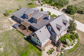 Aerial rear view of a 1.5-storey rural home in Midland, ON with Interlock weathered cedar shingle metal roofing, multiple dormers, chimney, and wood deck.