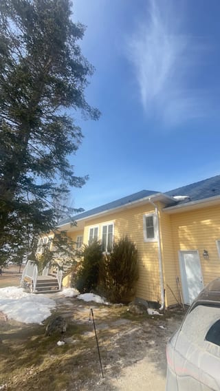 Deep Charcoal Interlock Cedar Shingle aluminum roof on a yellow ranch style home with a metal roof among tall pines, Wasaga Beach, Ontario