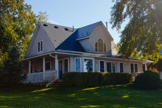 1.5-storey Craftsman home in Cannifton, ON with deep charcoal Interlock aluminum slate metal roof featuring dormers, wraparound porch, and arched upper window.