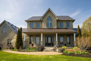 Two-storey Tudor-style stone home in Ariss, ON featuring Interlock Tudor Brown aluminum slate metal roofing with steep multi-pitch gables and Gothic arch window.