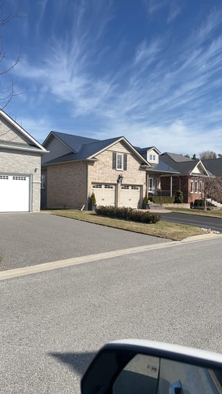 Street view of a 1.5-storey Craftsman-style brick home in Cobourg, ON featuring a black Interlock aluminum slate metal roof with multi-hip complexity.