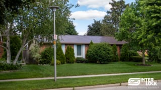 Single-storey ranch-style brick home with Interlock Colonial Brown cedar shingle aluminum roof, low-slope hip profile, lush landscaping.