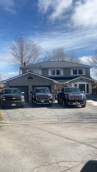 Two-storey brick Colonial home in Bradford, ON with black Interlock aluminum slate metal roofing, double garage, and three black trucks in the driveway.