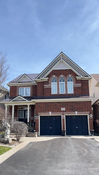 Two-storey brick Colonial home in Oshawa with Interlock aluminum slate roof in Colonial Brown, featuring multi-gable roofline and double navy garage doors.