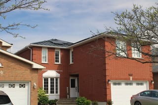 Two-storey red-brick suburban home with black Interlock aluminum standing seam metal roof featuring a low-pitch multi-hip profile, Mississauga ON.