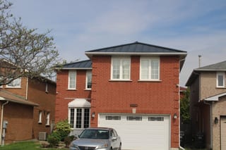 Two-storey red brick home in Mississauga with a low-pitch hip roof finished in black Interlock aluminum standing seam metal roofing.