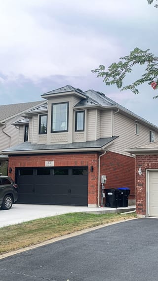 Two-storey brick home in Collingwood ON with Interlock deep charcoal aluminum slate metal roofing featuring a prominent front dormer and multi-hip roof.