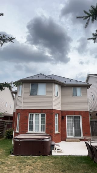 Rear elevation of a 2-storey brick-and-vinyl home in Collingwood, ON featuring an Interlock deep charcoal aluminum slate metal roof on a multi-hip structure.