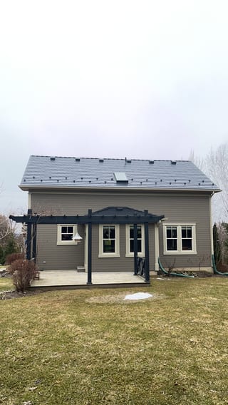 Rear elevation of a Craftsman-style home in Ravenna, ON featuring Interlock black aluminum slate metal roofing with snow guards, skylights, and a dark pergola over a rear patio.
