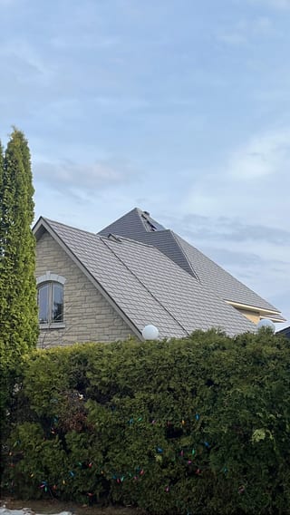 Tudor Brown Interlock Slate aluminum roof on a brown two-storey Tudor home with dormers among tall pines, Sudbury, Ontario