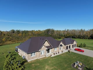 Tudor Brown Interlock Slate aluminum roof on a brown two-storey home with dormers among tall pines, Kawartha Lakes, Ontario